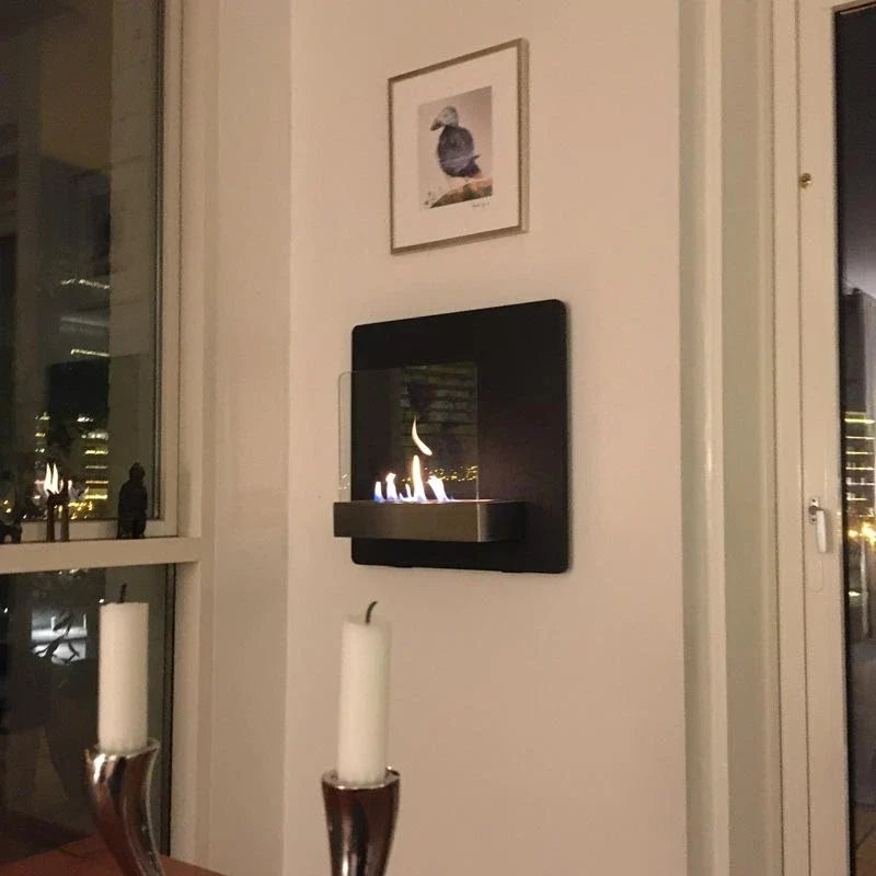 Black wall-mounted bioethanol fireplace lit in a modern living room at night, beside a window with a city view